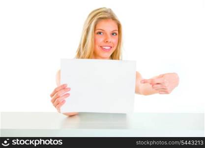 Smiling young girl sitting at table and pointing on blank paper&#xA;