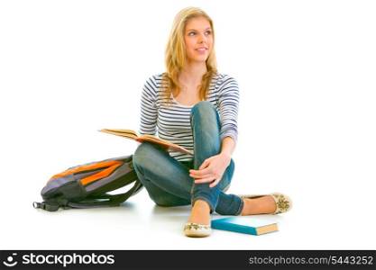 Smiling young girl sitting on floor with schoolbag and books and looking in corner at copy-space isolated on white &#xA;