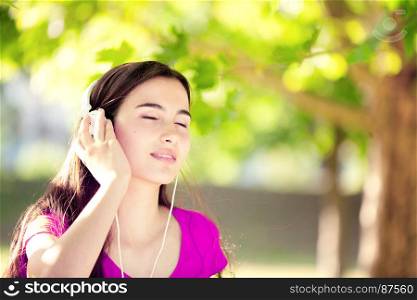 Smiling Young Girl with Pleasure Listening to Music on Headphones on a fine Autumn Day