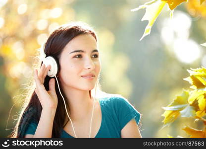 Smiling Young Girl with Pleasure Listening to Music on Headphones on a fine Autumn Day