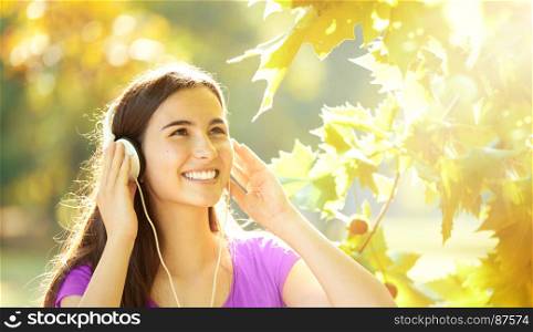 Smiling Young Girl with Pleasure Listening to Music on Headphones on a fine Autumn Day
