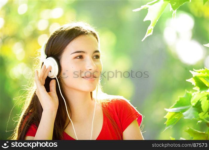 Smiling Young Girl with Pleasure Listening to Music on Headphones on a fine SpringDay