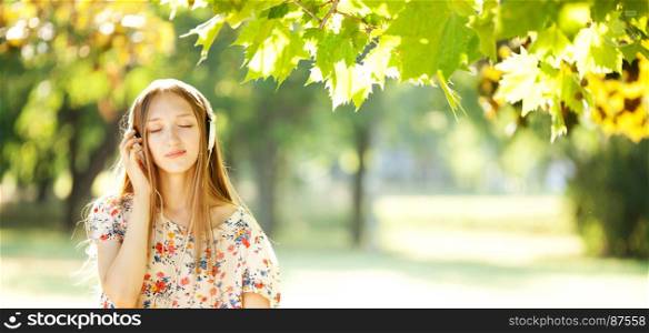 Smiling Young Girl with Pleasure Listening to Music on Headphones on a fine Summer Day