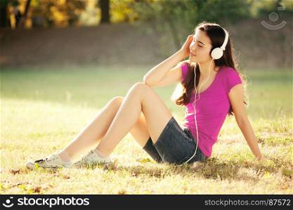Smiling Young Girl with Pleasure Listening to Music on Headphones with Closed Eyes on a fine Autumn Day