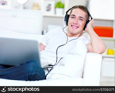 Smiling young guy listening music in headphone from laptop at home