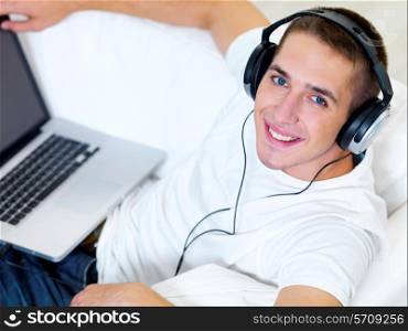 Smiling young guy listening music on the laptop with headphone at home - high angle