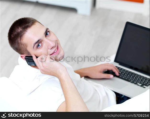 smiling young guy using mobile phone and laptop at home