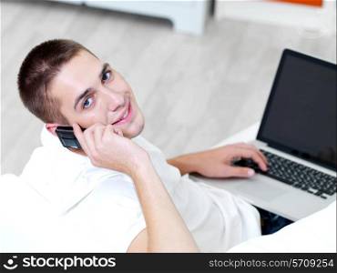 smiling young guy using mobile phone and laptop at home