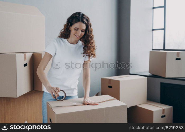 Smiling young hispanic woman using adhesive tape, packing carton parcel box. Female moving service worker holding duct tape preparing belongings to relocation day. Delivery, removal concept.. Female using adhesive tape, packing carton parcel box. Advertising of removal service, delivery