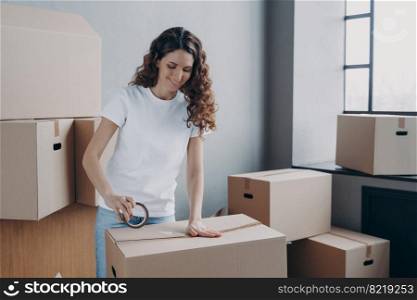 Smiling young hispanic woman using adhesive tape, packing carton parcel box. Female moving service worker holding duct tape preparing belongings to relocation day. Delivery, removal concept.. Female using adhesive tape, packing carton parcel box. Advertising of removal service, delivery