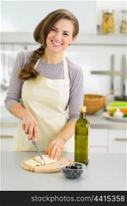 Smiling young housewife cutting fresh cheese
