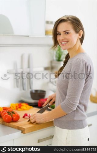 Smiling young housewife cutting vegetables on salad in kitchen