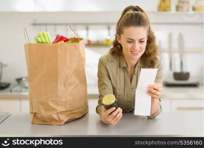 Smiling young housewife examines purchases and check after shopping in kitchen