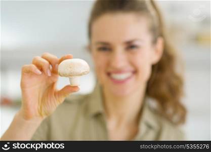 Smiling young housewife holding mushroom in kitchen