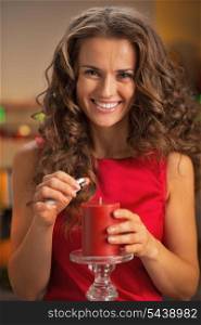 Smiling young housewife lighting candle in christmas decorated kitchen