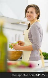 Smiling young housewife mixing salad in modern kitchen