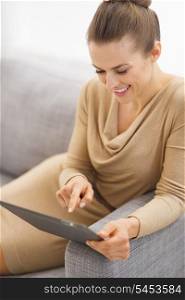 Smiling young housewife sitting on couch and using tablet pc