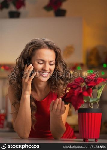 Smiling young housewife talking phone and playing with christmas rose