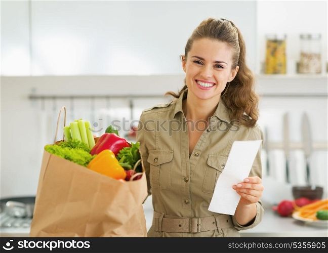 Smiling young housewife with check and shopping bag full of vegetables