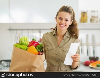 Smiling young housewife with check and shopping bag full of vegetables