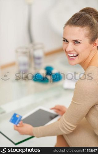 Smiling young housewife with credit card using tablet pc in living room