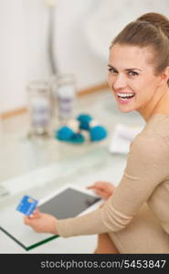 Smiling young housewife with credit card using tablet pc in living room