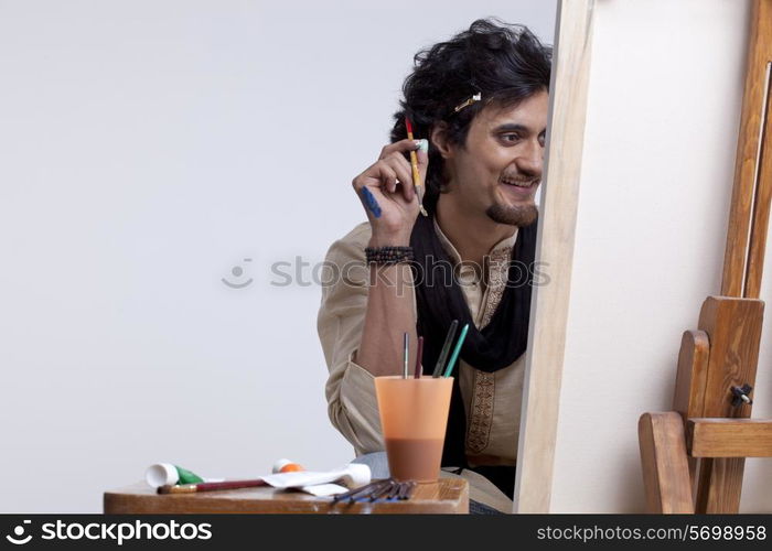 Smiling young male artist holding paintbrush against colored background