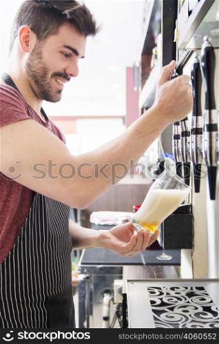 smiling young male bartender pours fresh light beer from tap