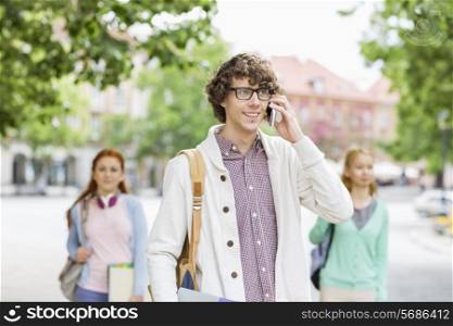 Smiling young male student using cell phone with friends in background on street