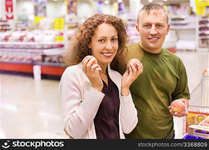 Smiling young man and woman buy peaches in supermarket