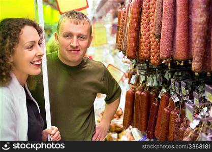 Smiling young man and woman buy sausage in supermarket