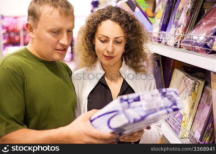 Smiling young man and woman buying bedding in supermarket, looking on bedding