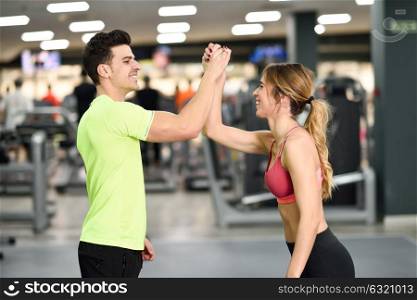 Smiling young man and woman doing high five in gym. Couple wearing sportswear