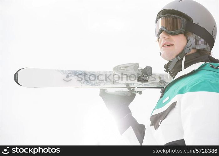 Smiling young man carrying skis against clear sky