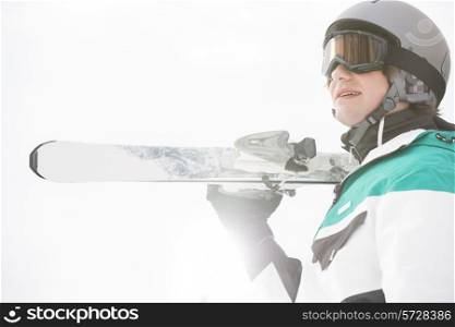Smiling young man carrying skis against clear sky