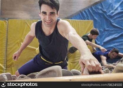 Smiling young man climbing up a climbing wall in an indoor climbing gym, directly above