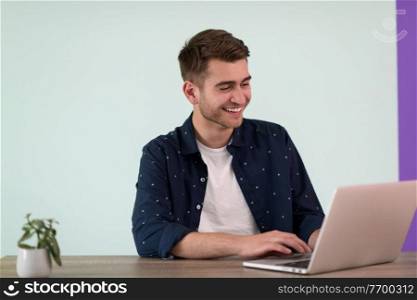 Smiling young man freelancer using laptop studying online working from home, happy casual millennial guy typing on pc notebook surfing internet 

