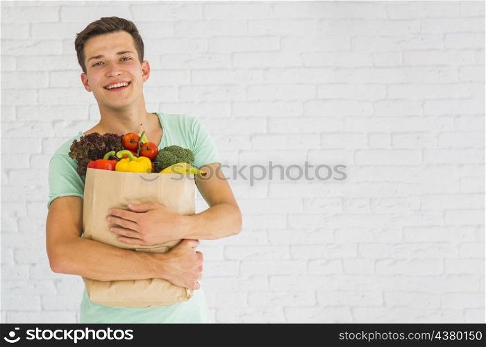 smiling young man holding fresh vegetables fruits grocery paper bag