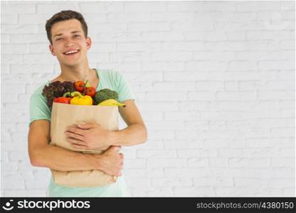 smiling young man holding fresh vegetables fruits grocery paper bag