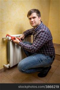 Smiling young man holding pliers and installing radiator valve