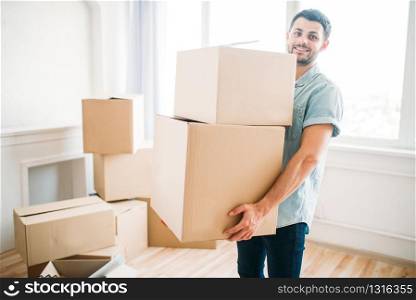 Smiling young man holds cardboard boxes in hands, housewarming. Moving to new house