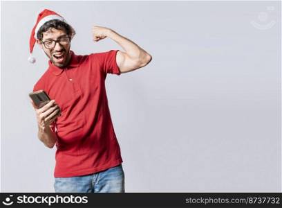 Smiling young man in christmas hat using cellphone celebrating. Happy guy in christmas hat looking at cellphone and celebrating excited. People in santa hat looking at cell phone excited