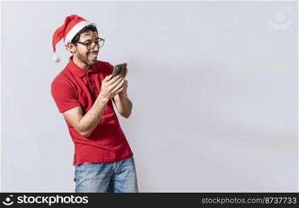 Smiling young man in christmas hat using cellphone isolated. Happy guy in christmas hat smiling at cellphone isolated. People in santa hat using and smiling at cellphone isolated