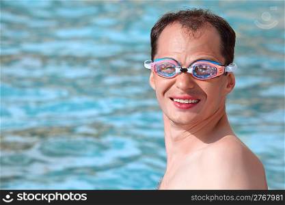 smiling young man in watersport goggles swimming in pool