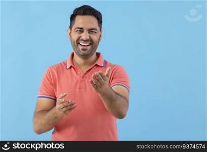 Smiling young man looking and pointing at camera against blue background