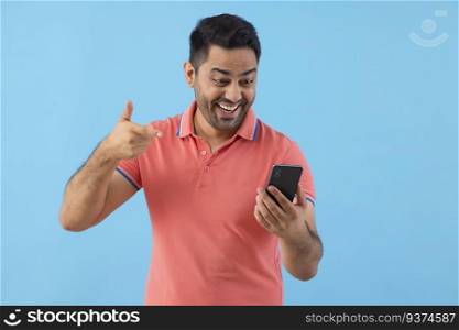 Smiling young man looking and pointing at Smartphone holding in his hand 