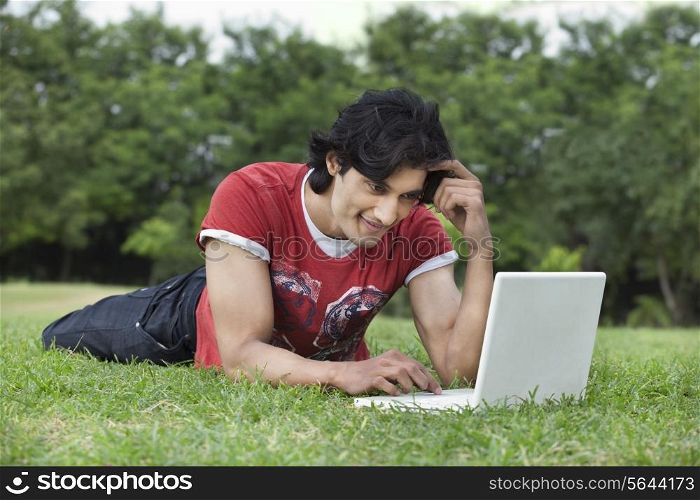 Smiling young man lying on grass using laptop