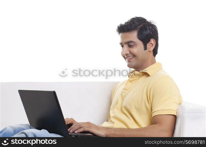 Smiling young man on sofa using laptop