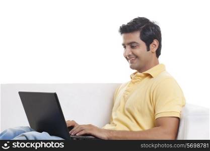 Smiling young man on sofa using laptop