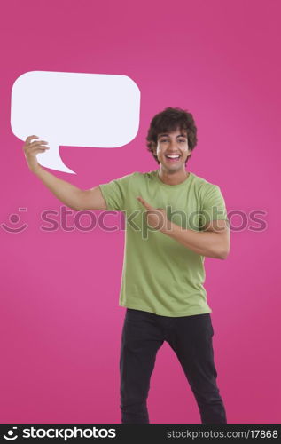 Smiling young man pointing at speech bubble over pink background